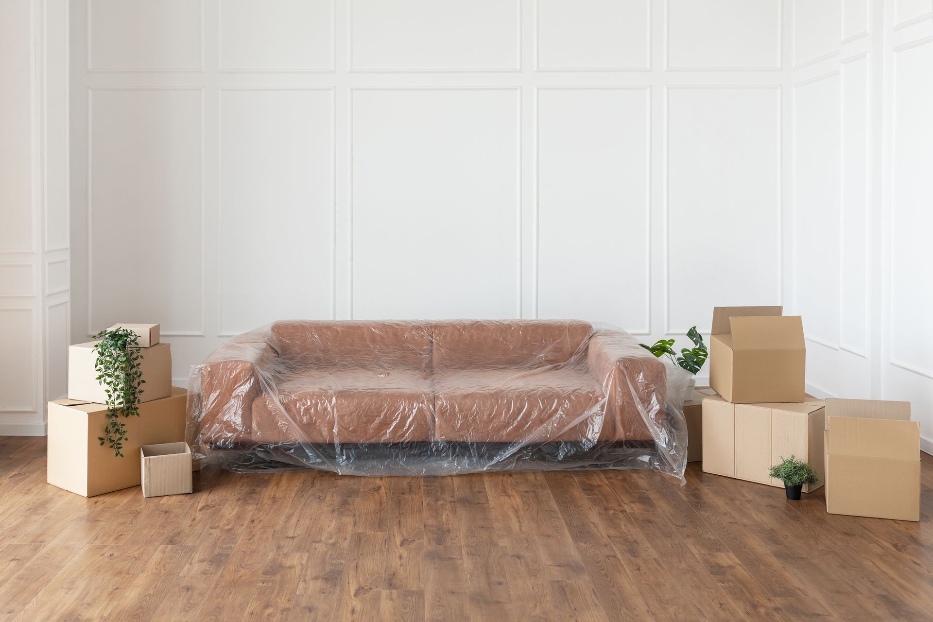 Brown sofa with plastic cover, and boxes in an empty room, showcasing a furniture storage service.