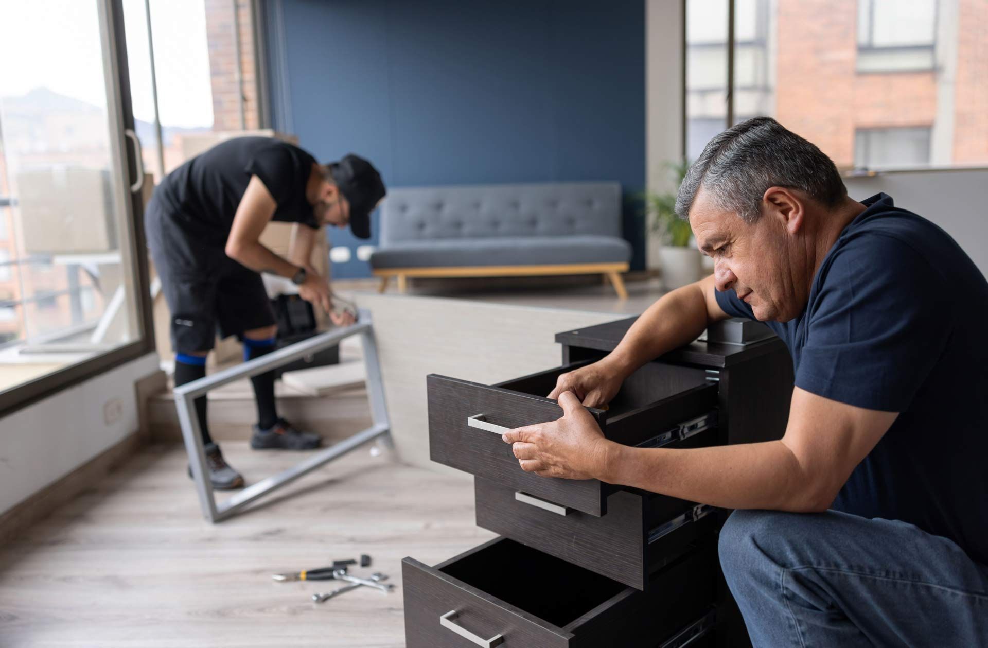 Two men assembling furniture in a modern living room with large windows. Two men assembling furniture in a modern living room with large windows.