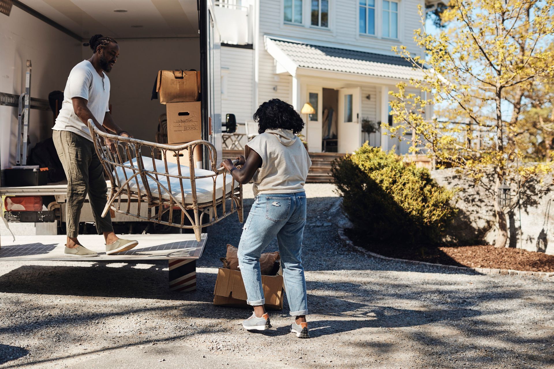 Workers performing residential furniture removal, loading sofa into moving truck outside home.