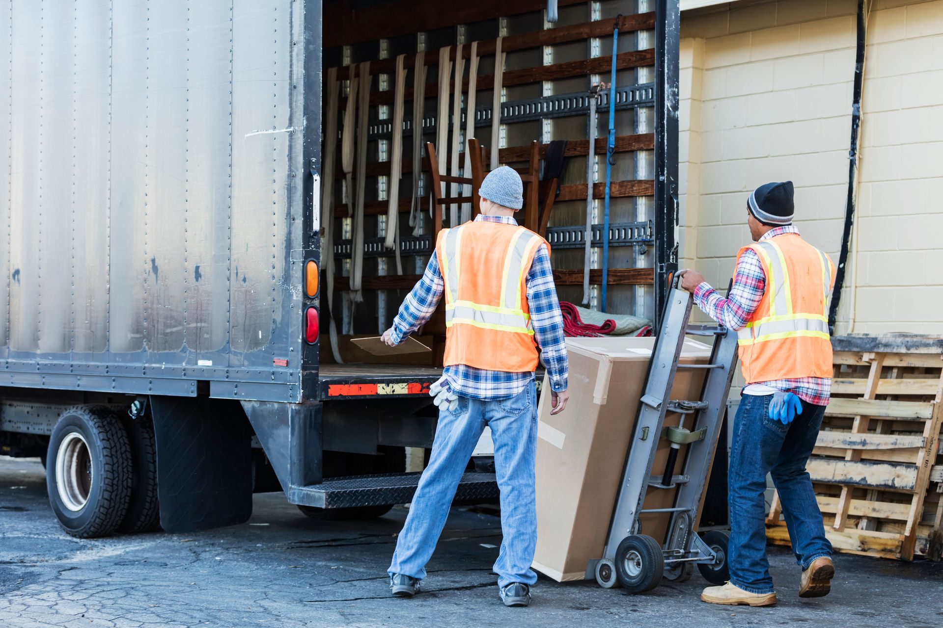 Two workers, in reflective vests at the back of a truck, performing commercial furniture removal.