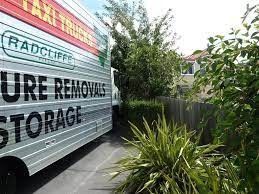 A man is carrying a couch in front of a moving truck.