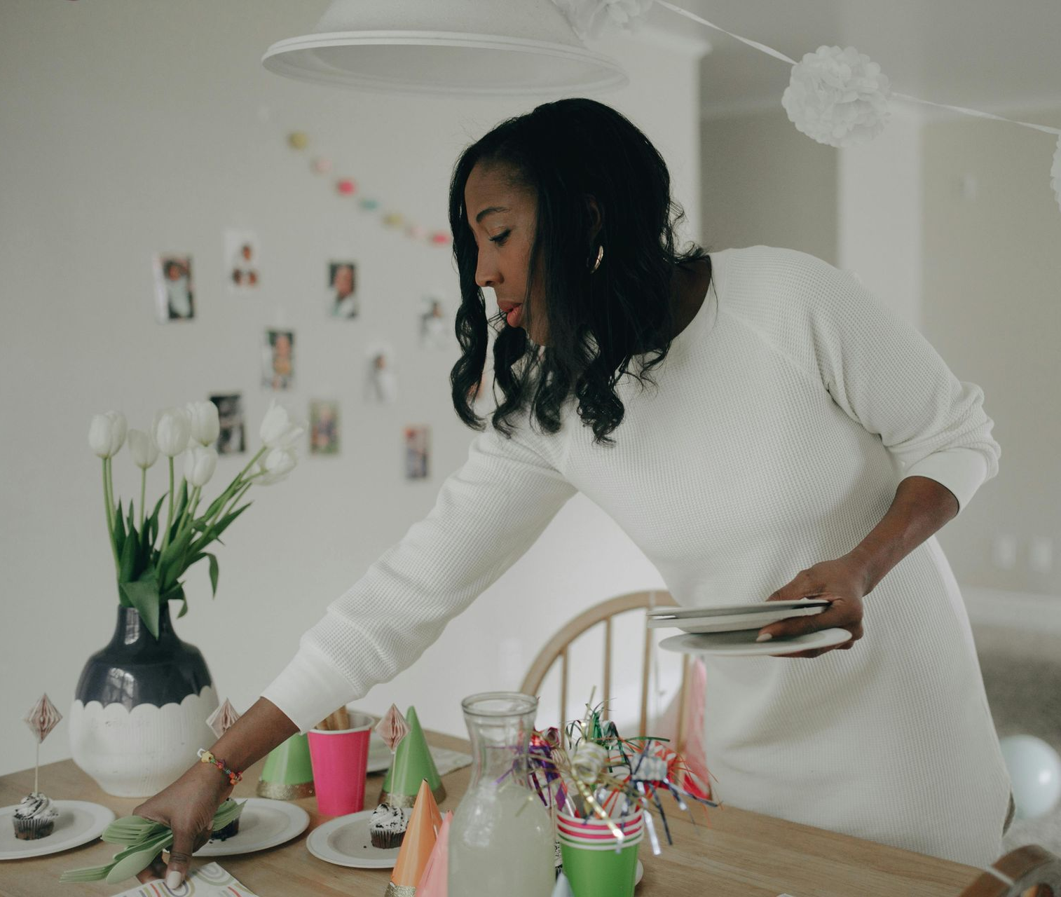 A woman is arranging plates on a party table set with cupcakes, decorations, and flowers.