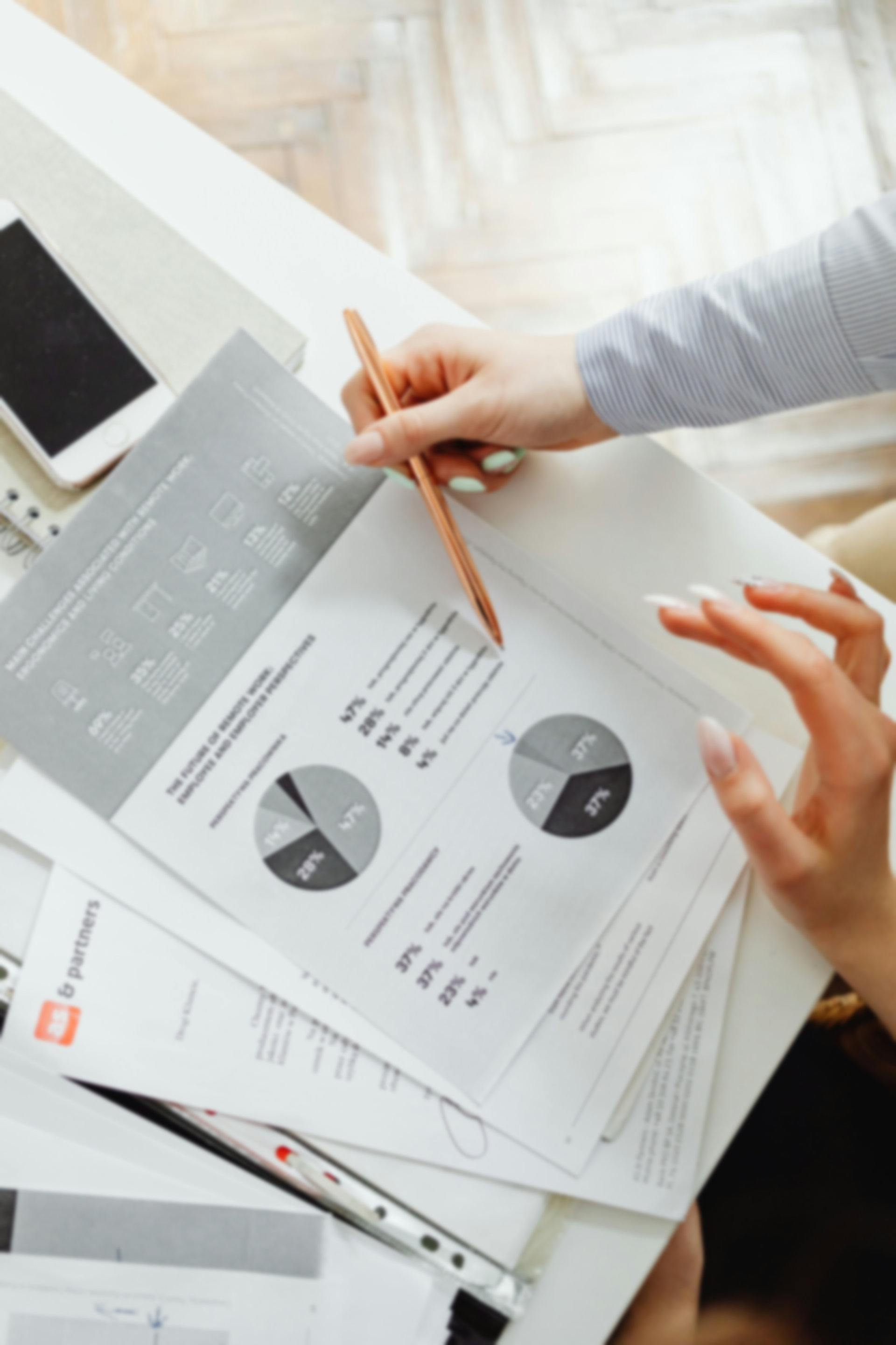A person pointing at a pie chart on a report, likely reviewing data at a desk.  A tablet and other papers are also visible.