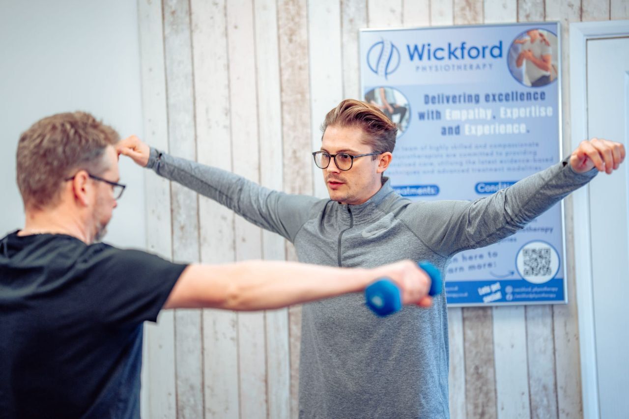 A man is lifting a blue dumbbell in front of a sign that says wickford.