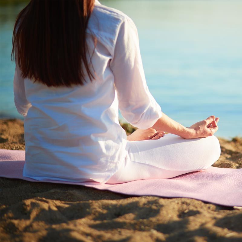A woman is sitting on a yoga mat on the beach