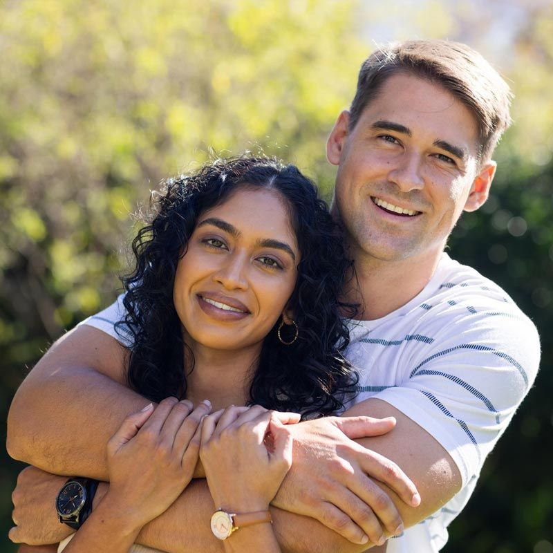 A man and a woman are hugging each other and smiling for the camera.