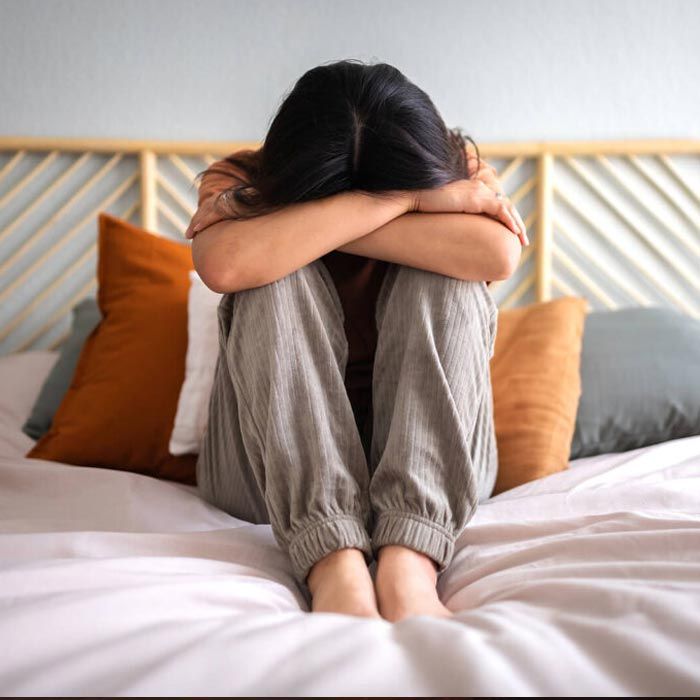 A woman is sitting on a bed with her head down
