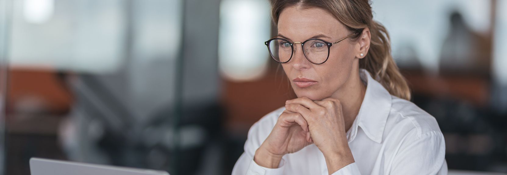 A woman wearing glasses is sitting in front of a laptop computer.