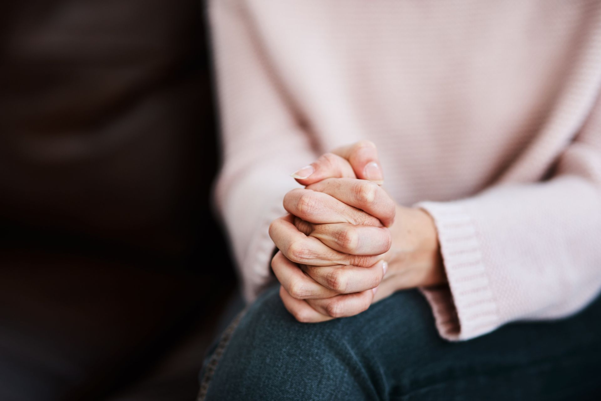 A woman is sitting on a couch with her hands folded in prayer.
