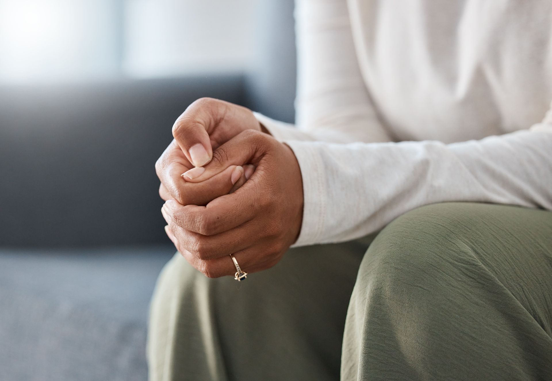 A woman is sitting on a couch with her hands folded in prayer.