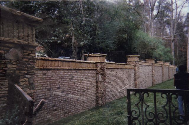 A brick wall surrounds a lush green field with trees in the background.