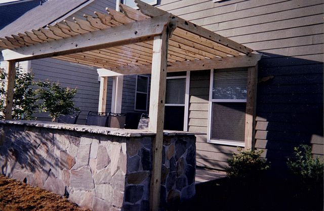 A house with a stone wall and a wooden pergola