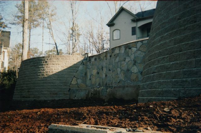 A large stone wall with a house in the background