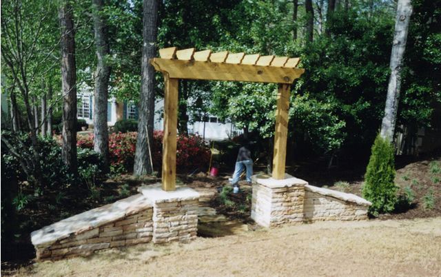 A wooden pergola is in the middle of a lush green forest.