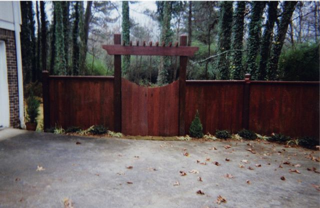 A wooden fence surrounds a driveway with trees in the background