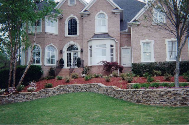 A large brick house with a stone wall in front of it