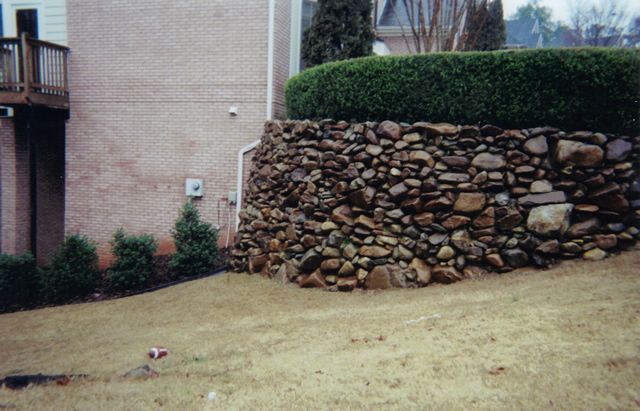 A large rock wall in front of a brick house