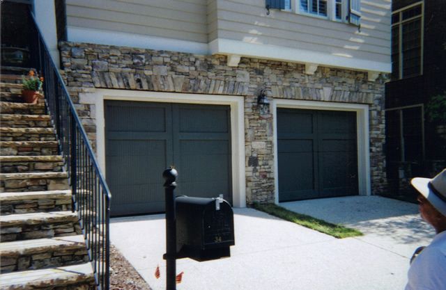 A man in a hat stands in front of a house with two garage doors