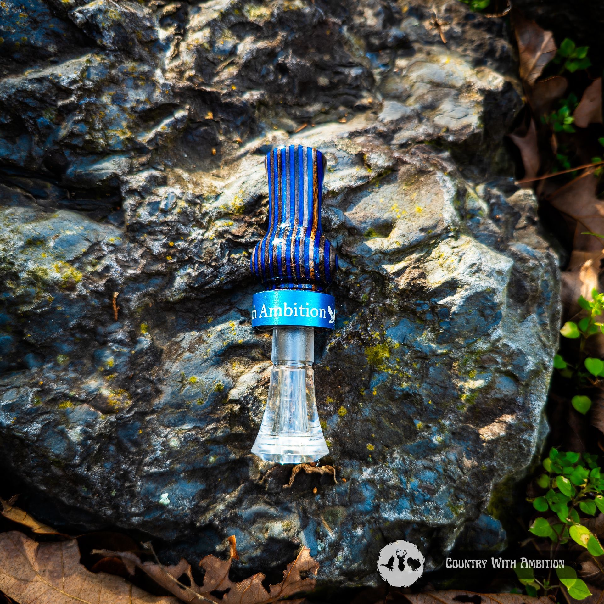 Blue hand turned duck call on a rough, blue-gray rock. Blue Country With Ambition band.