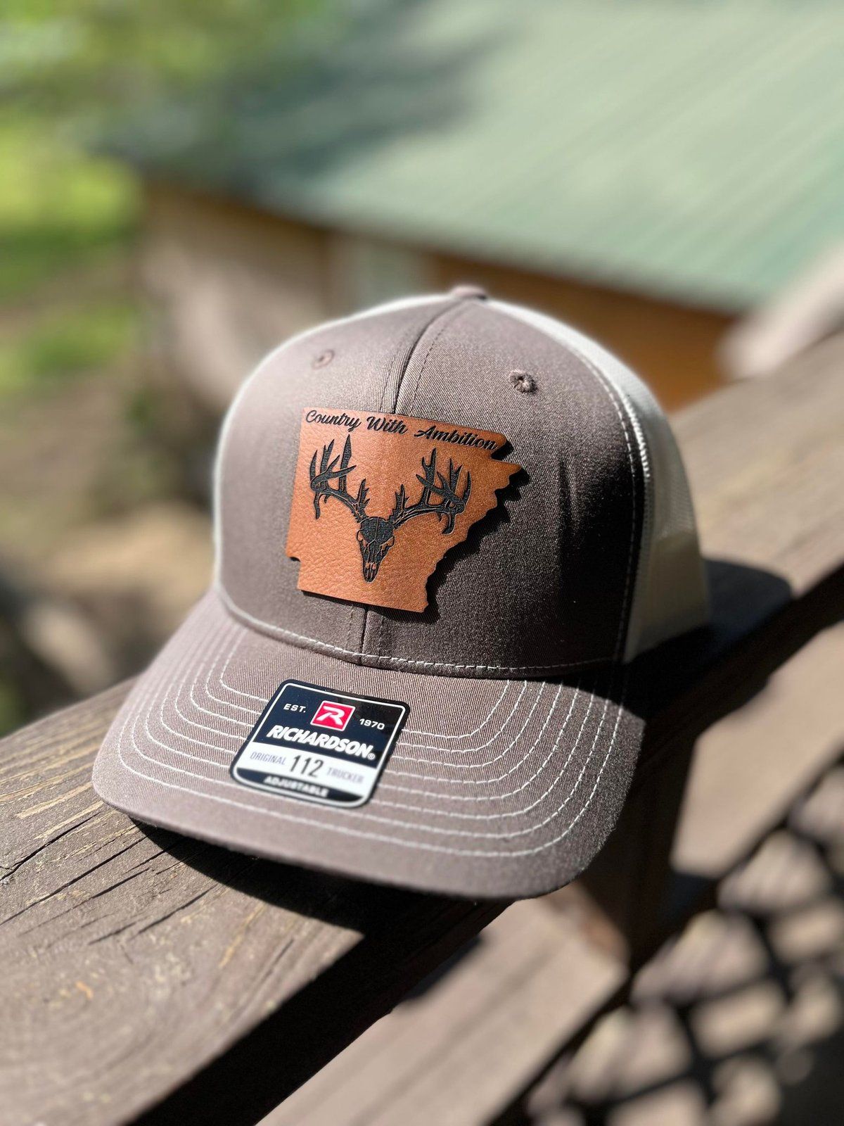Brown and white cap with an Arkansas state cutout and buck silhouette from Country With Ambition.
