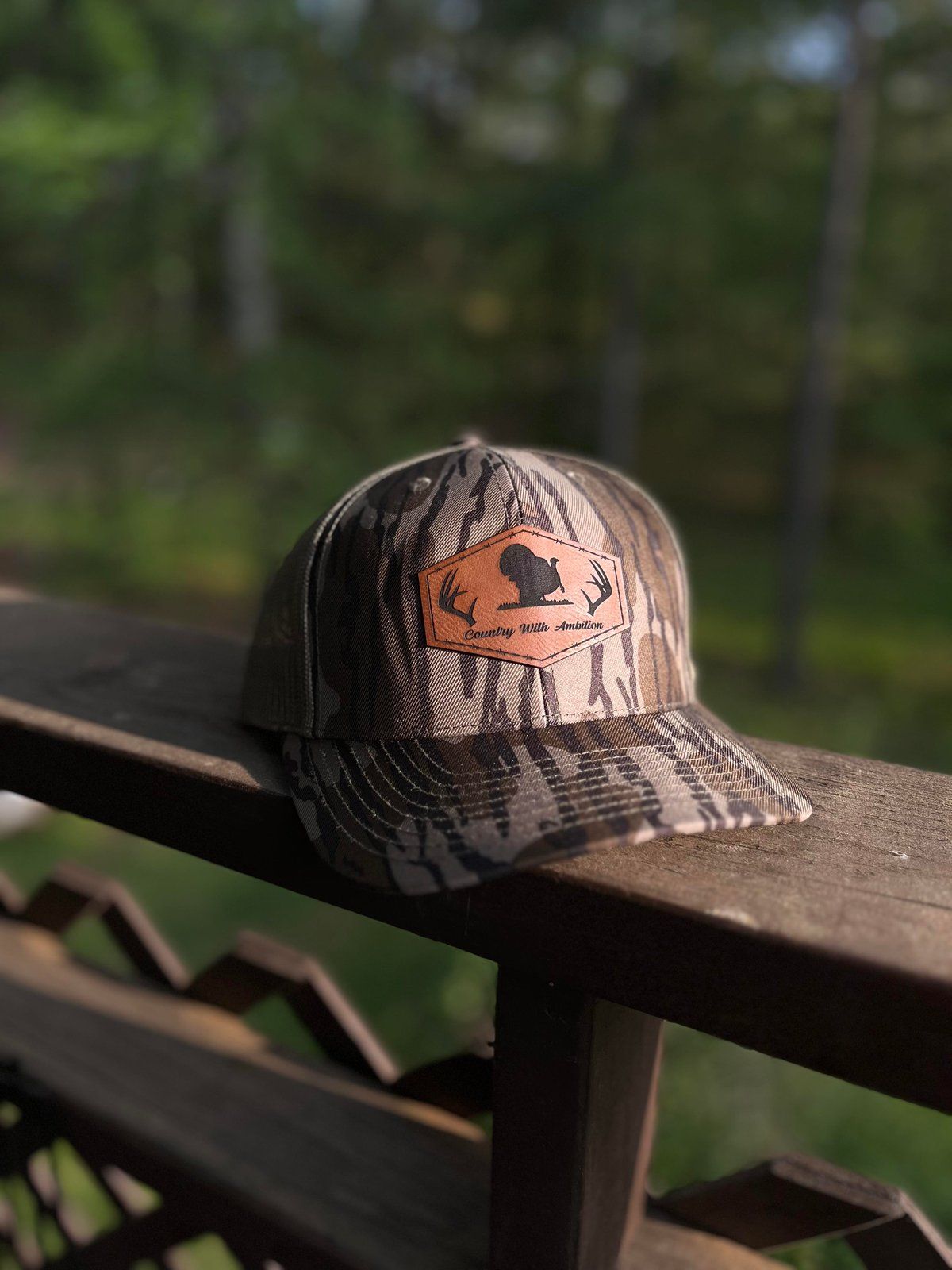 Camouflage trucker hat with orange patch on a wooden railing, outdoors.