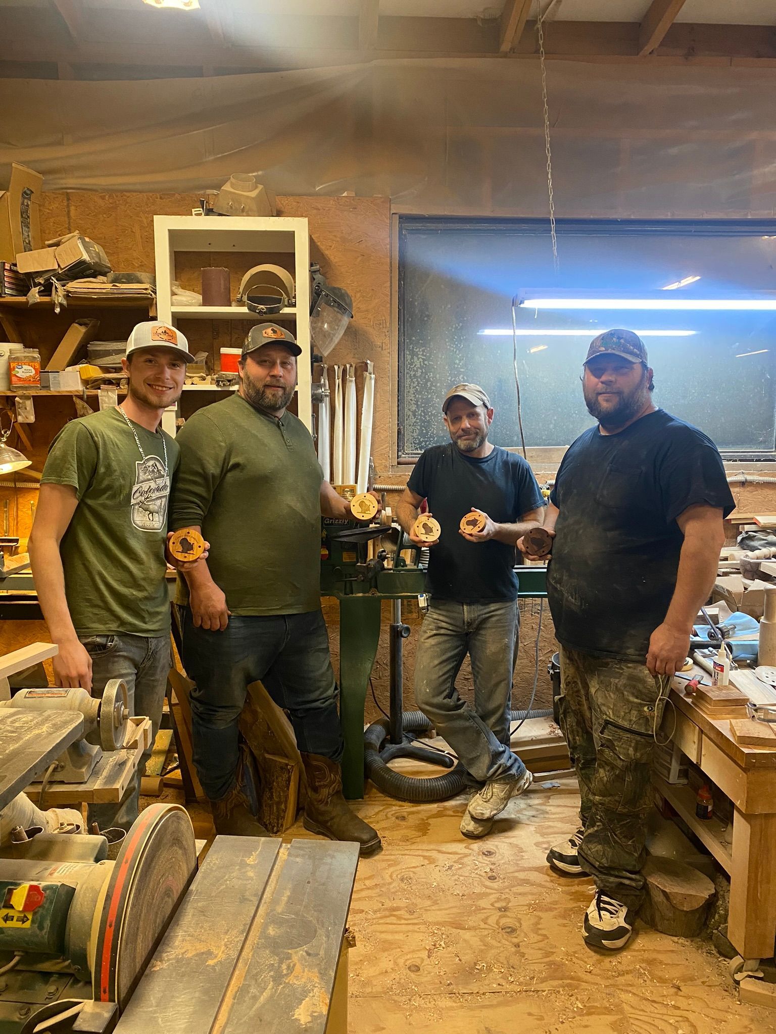 Four men in a workshop holding wooden hand turned turkey pot calls.