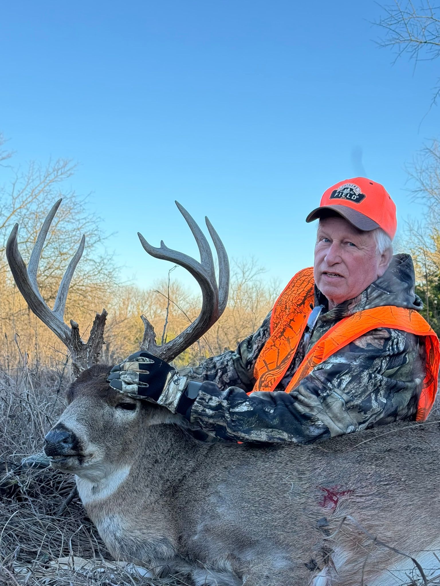 Hunter in orange vest with a large buck. Winter setting, blue sky. Man holding the deer's antlers.