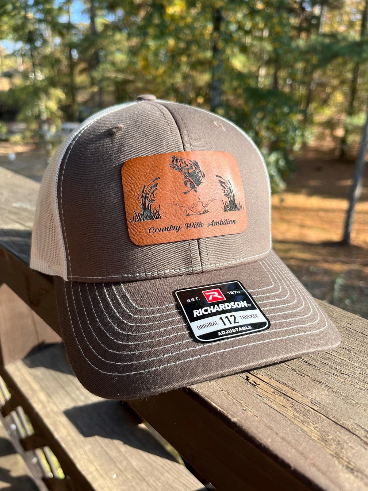 Brown and white trucker hat with a leather patch featuring bass; Richardson Country With Ambition