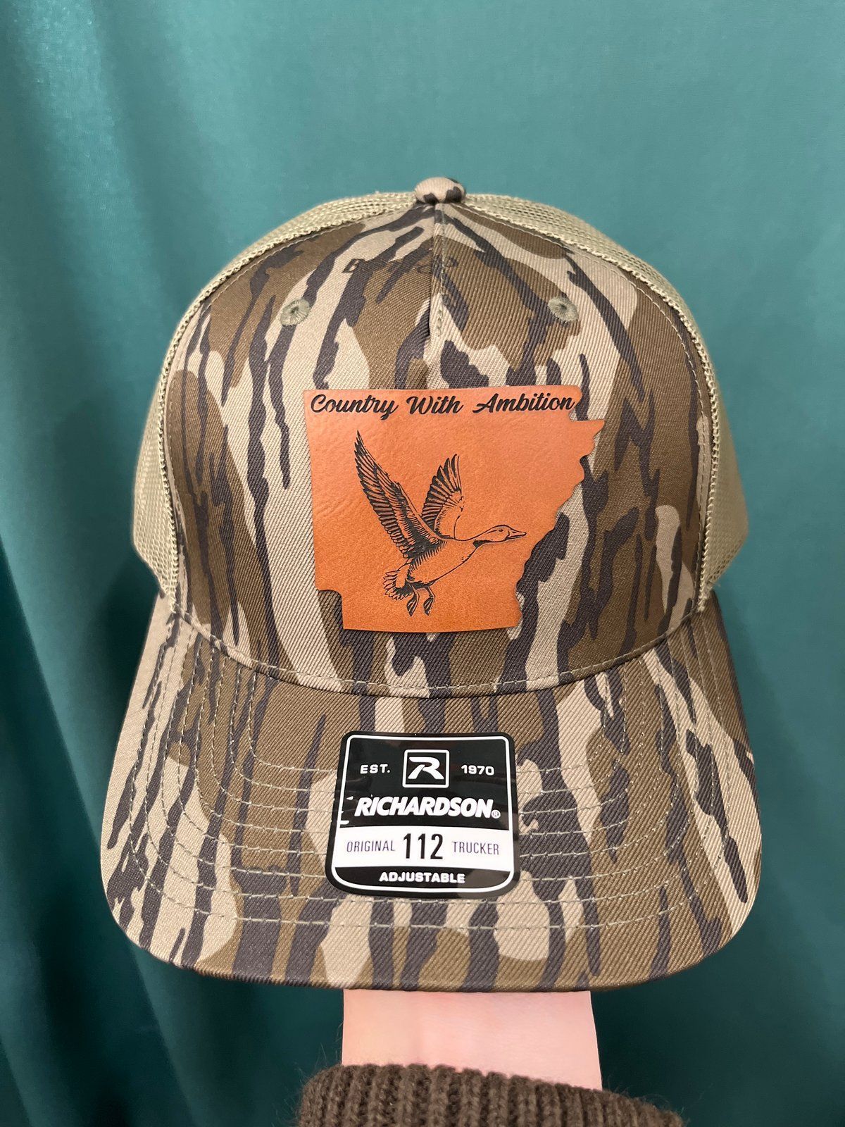 Gray and white Richardson trucker hat with a leather duck patch
