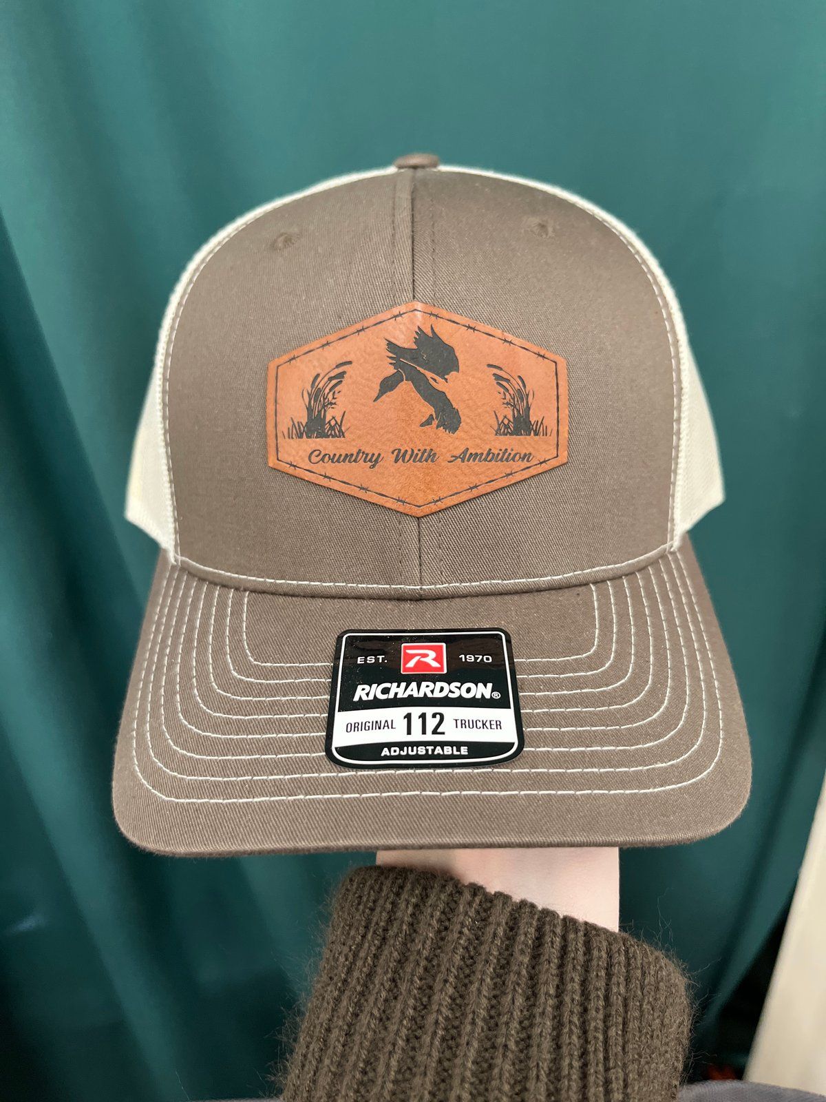Brown and beige Richardson trucker hat with a leather duck patch