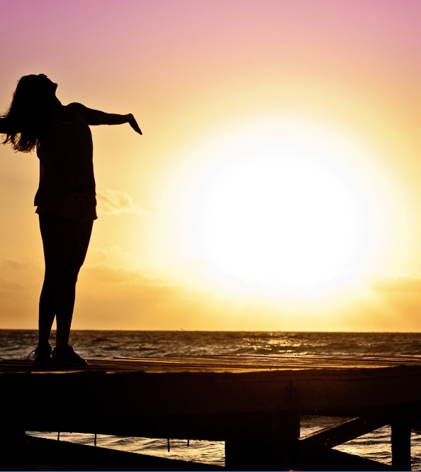 Woman looking into sunrise with arms wide open
