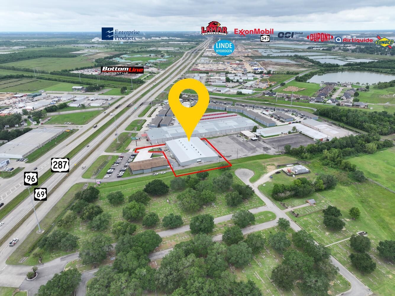 Aerial view of a commercial building with a yellow location marker; highway and nearby businesses visible.