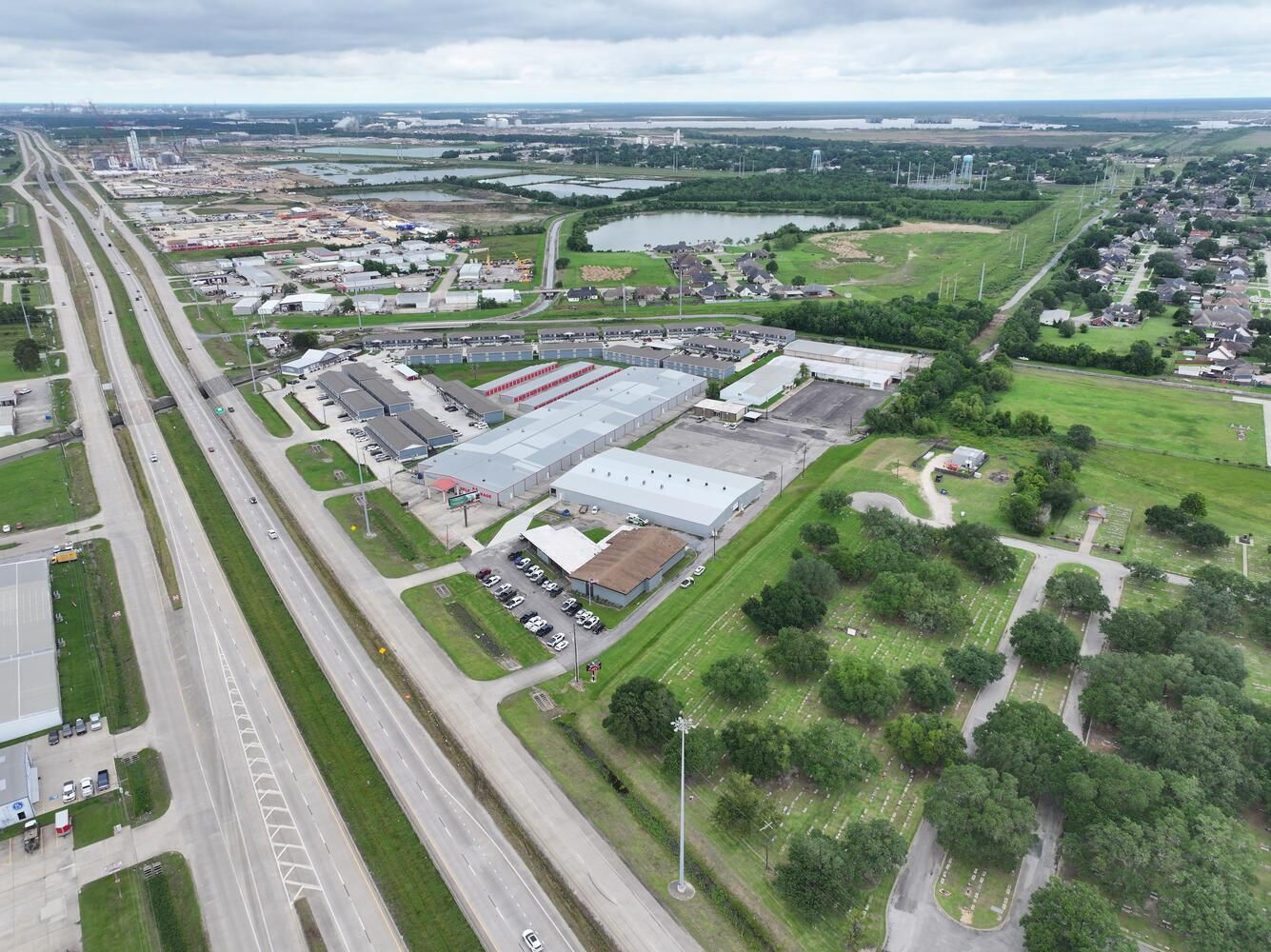 Aerial view of a highway, businesses, and green spaces in an urban setting under a cloudy sky.