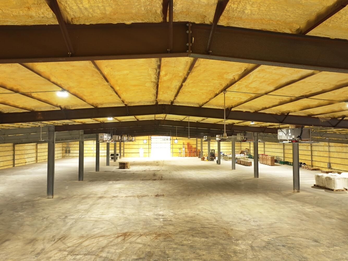 Interior view of an empty warehouse with exposed steel beams, insulation, and concrete floor.