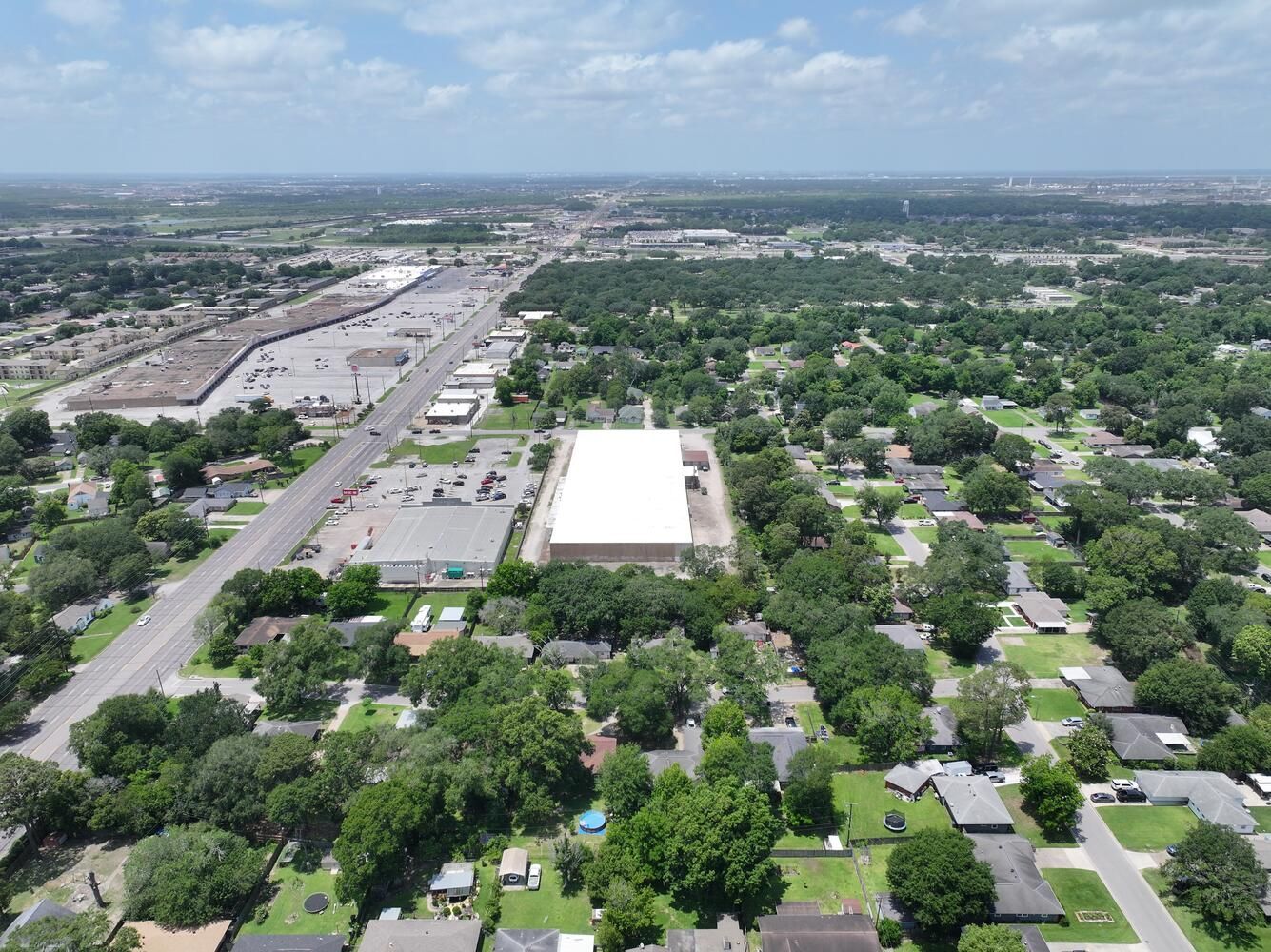 Aerial view of a suburban area with a large white-roofed building, trees, roads, and businesses under a blue sky.