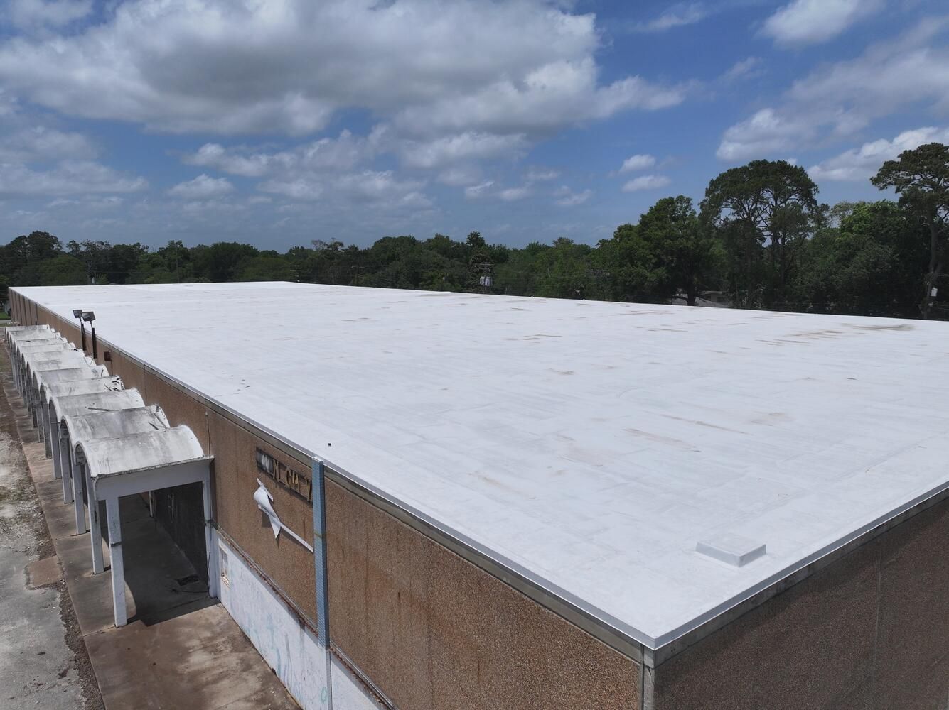 Flat white commercial roof on a brick building, surrounded by trees under a cloudy sky.
