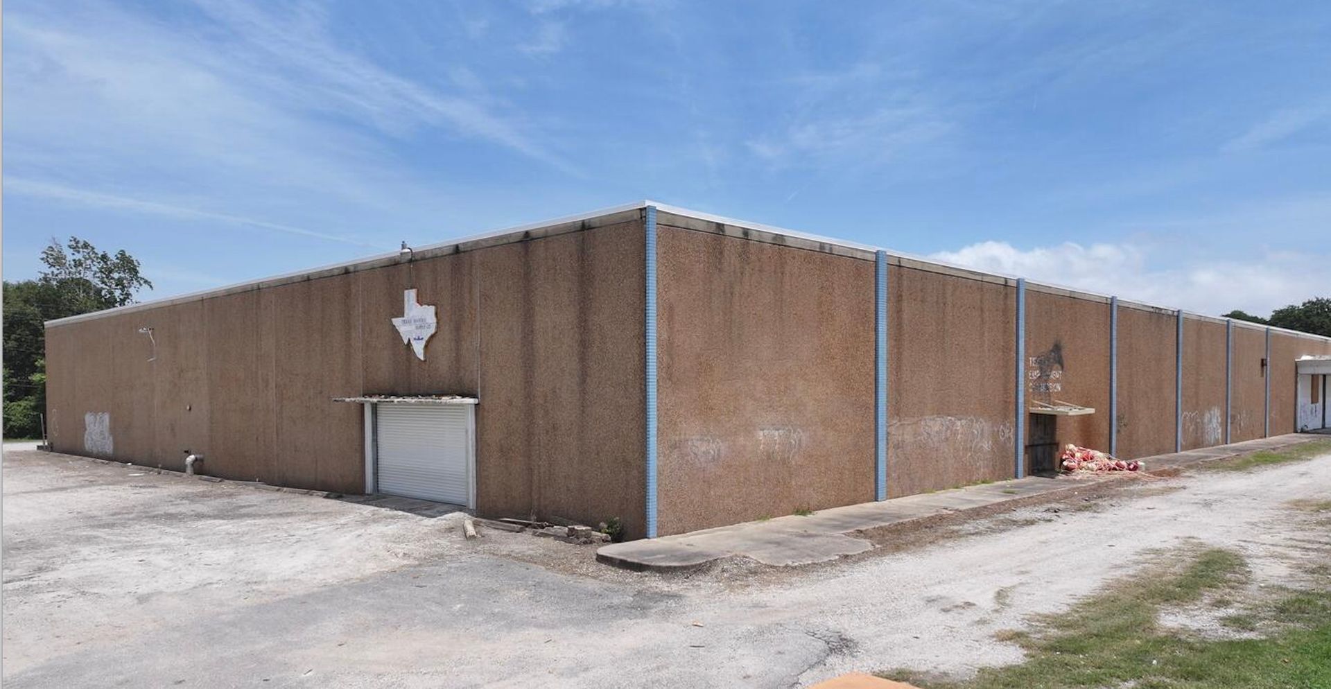A brown building with a Texas star, blue sign, and driveway under a cloudy sky.