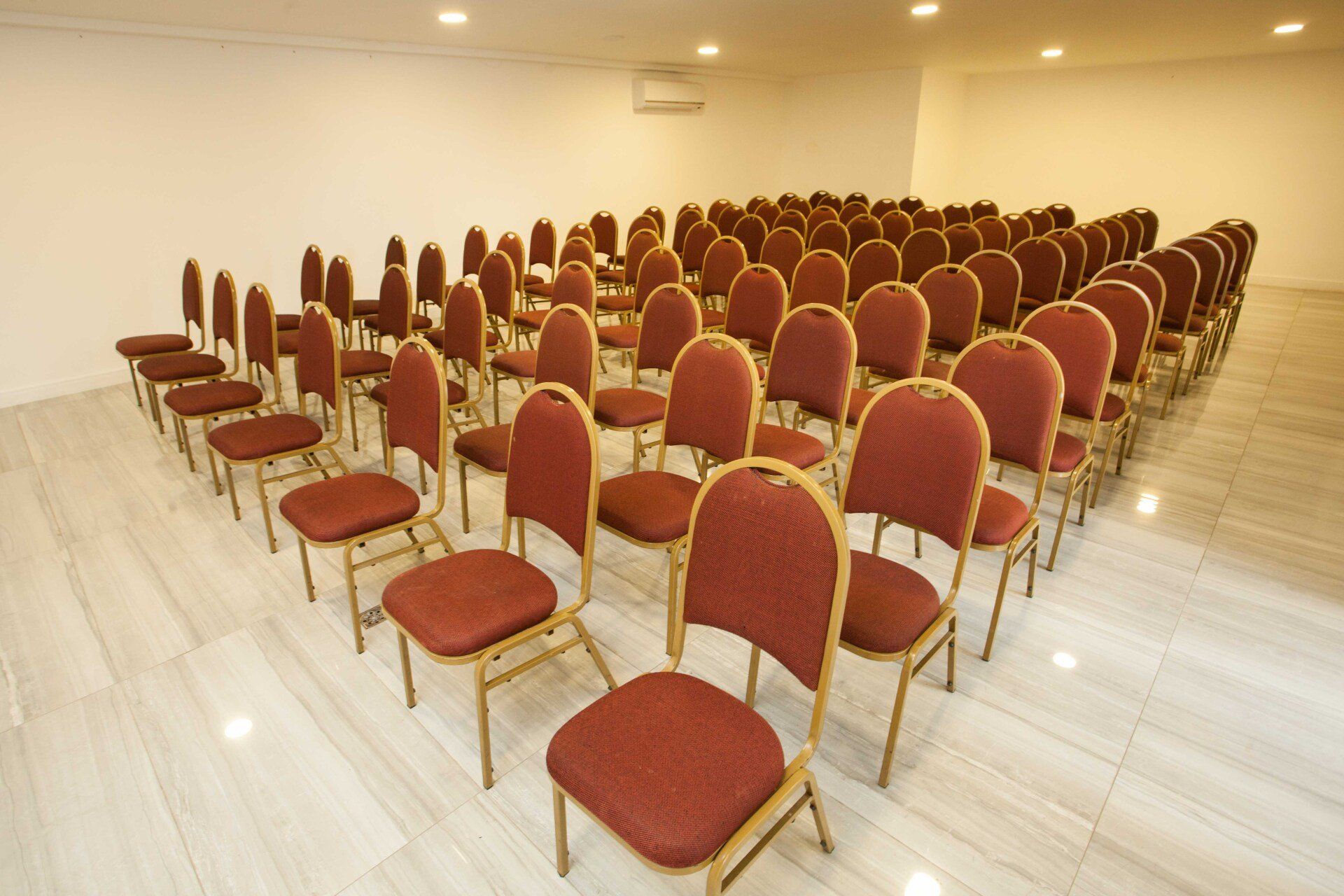 Fileiras de cadeiras vermelhas estão alinhadas em uma sala de conferências.