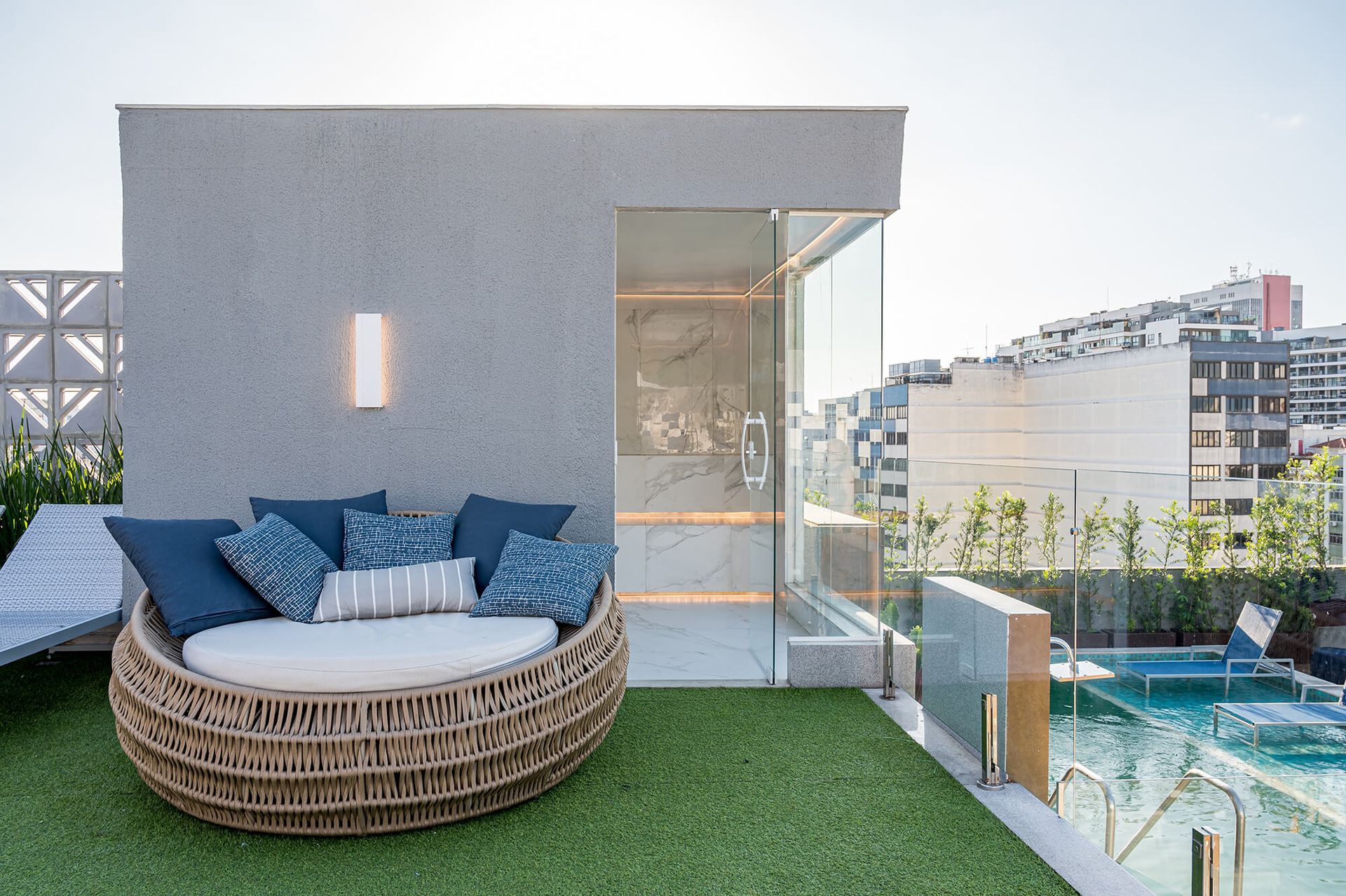 Um sofá redondo está sobre um gramado verdejante ao lado de uma piscina.