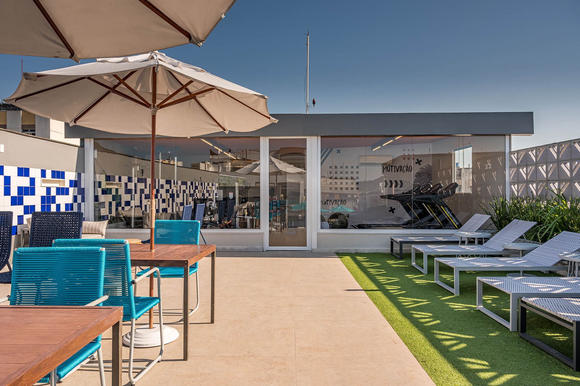 Um pátio com mesas, cadeiras e guarda-sóis em frente a uma academia.