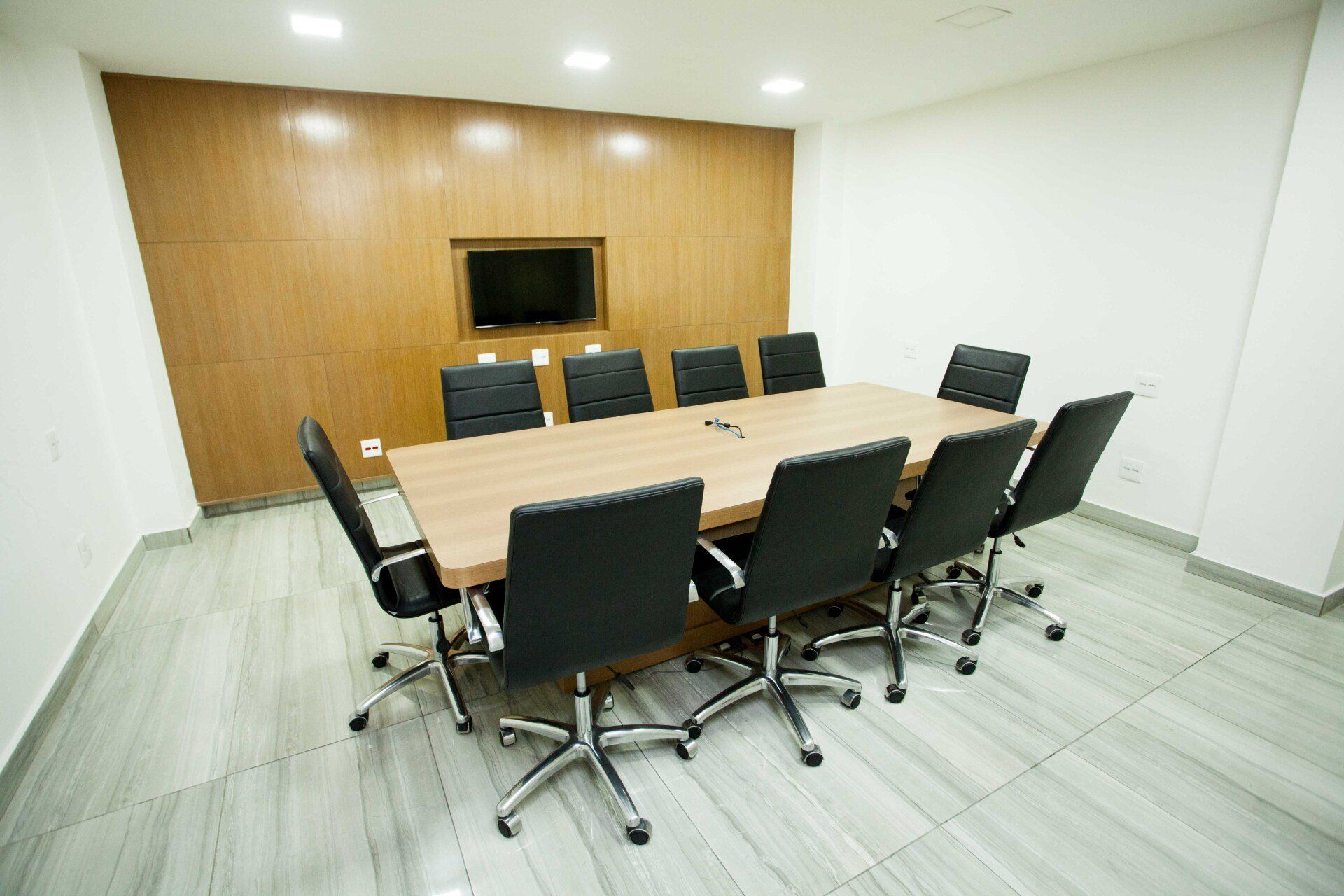 Uma sala de conferências com uma mesa longa, cadeiras e uma TV de tela plana.