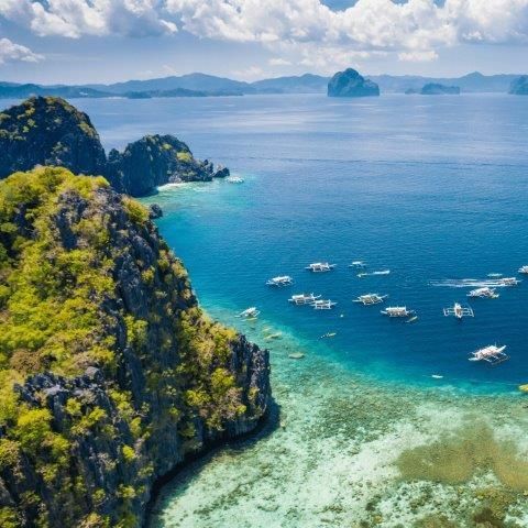 Island coast with turquoise water, boats, and limestone cliffs under a blue sky.
