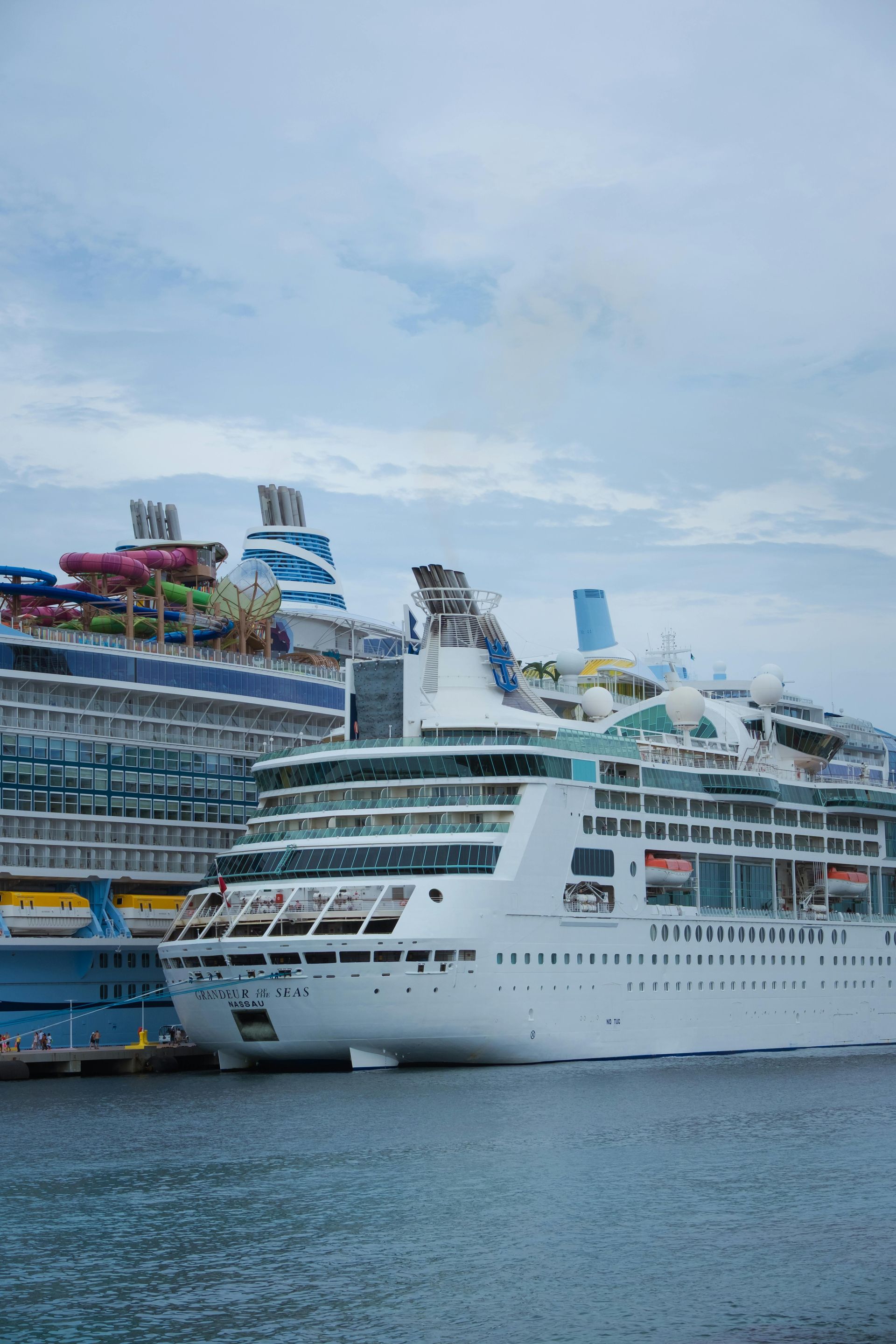 Cruise ships docked in a harbor. White and blue vessels against a cloudy sky.