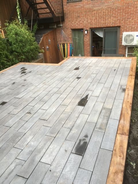 Une terrasse en briques avec une bordure en bois devant un bâtiment en briques.