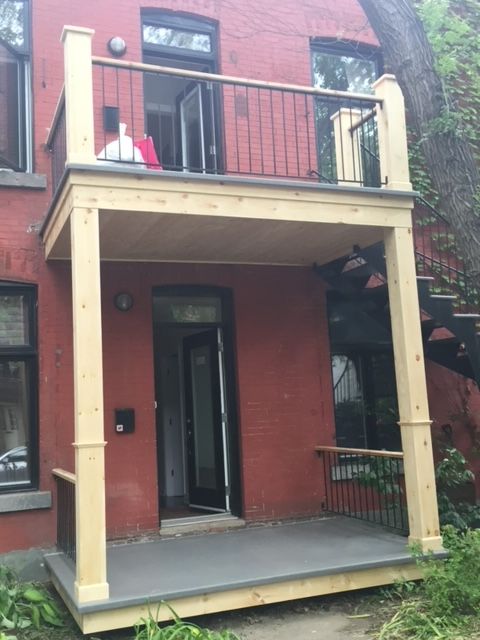 Une maison en briques rouges avec un porche et un balcon en bois