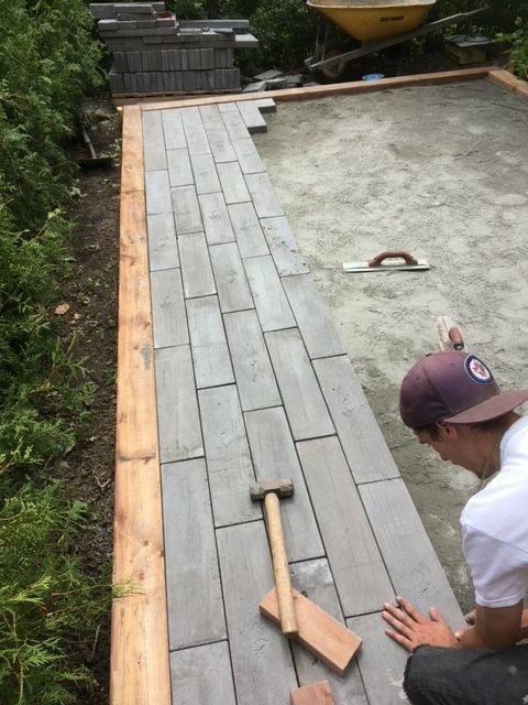 Un homme travaille sur une allée en briques avec un marteau et une truelle.