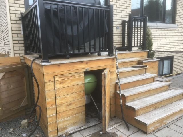 Une terrasse en bois avec des escaliers et un gril en dessous.
