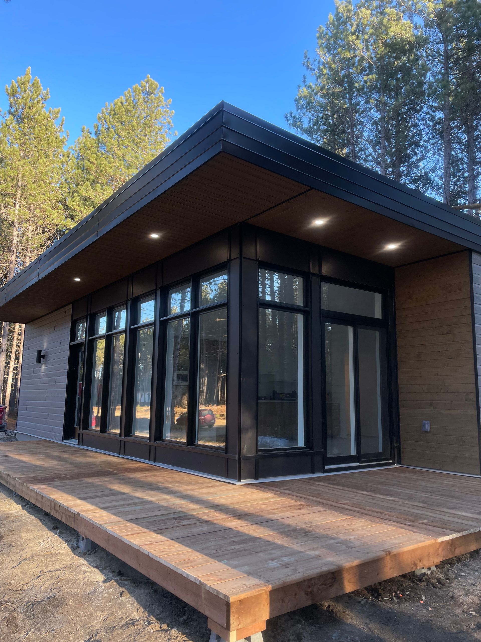 Une petite maison avec beaucoup de fenêtres et une terrasse en bois.