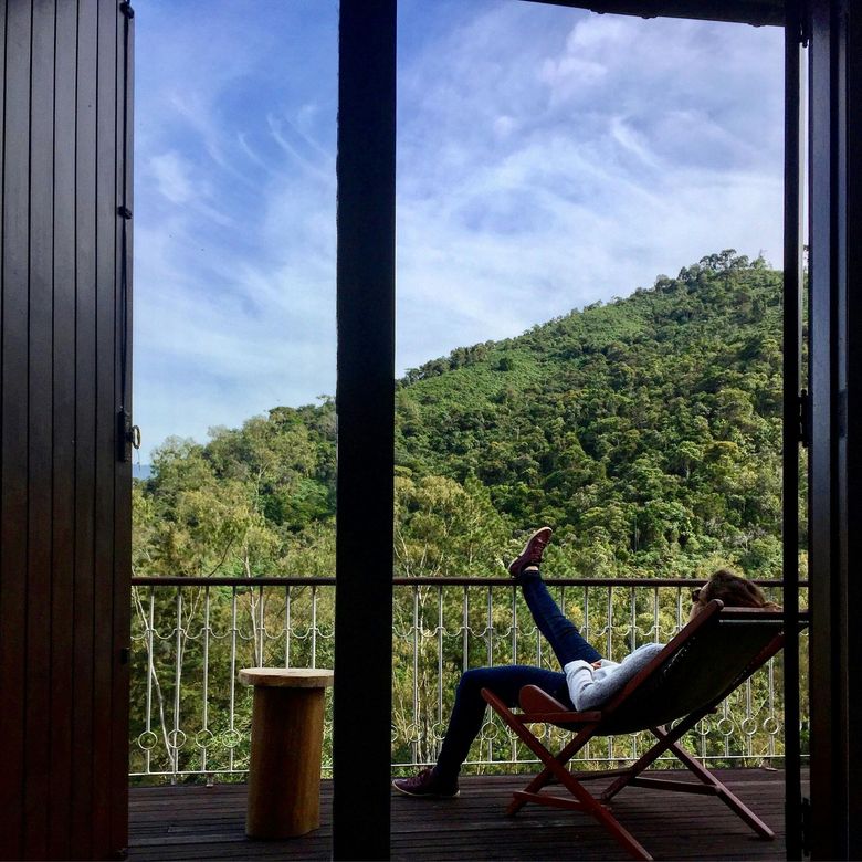 Une femme est allongée sur une chaise sur un balcon donnant sur une forêt