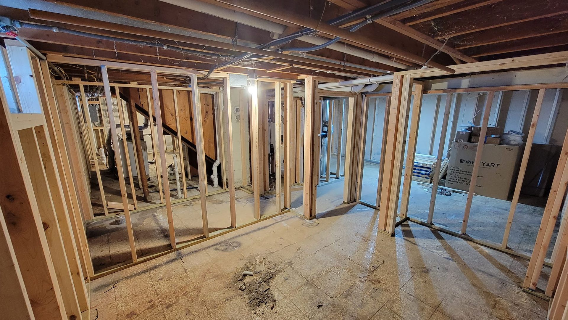 The interior of an unfinished basement shows wooden wall framing studs being installed on a concrete floor.